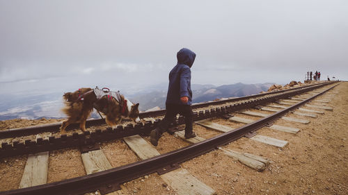 Rear view of woman standing by railroad tracks against sky during winter