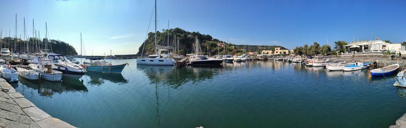 Boats moored at harbor against blue sky