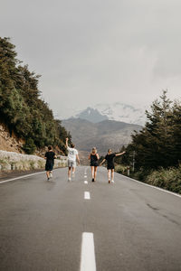 Rear view of friends walking on road against sky