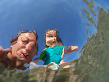 Low angle view of father and daughter seen through water in sea against blue sky