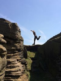 Full length side view of woman balancing on rock formation against sky at stanage edge