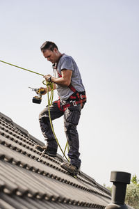 Craftsman with power tool holding rope standing on roof