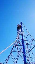 Low angle view of girl on top of rope pyramid in park against clear blue sky