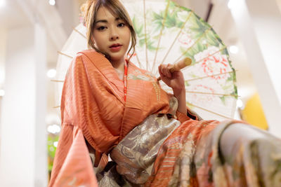 Portrait of young woman holding umbrella sitting at mall