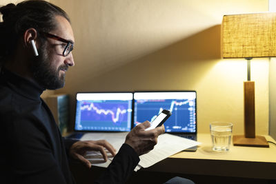 Trader with in-ear headphones using smart phone at home office