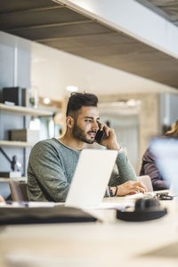 Male entrepreneur talking on smart phone while working at table in office