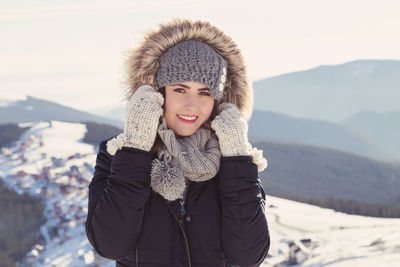 Cheerful woman wearing fur coat while standing against mountains during winter