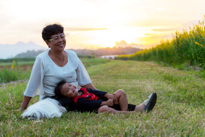 Portrait of smiling girl with grandmother and dog on grass during sunset