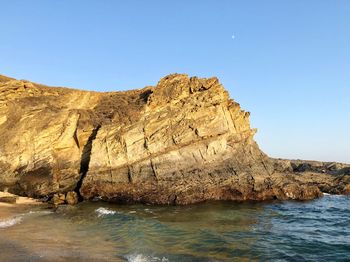 Rock formations in sea against clear blue sky