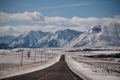 Empty road by snowcapped mountains against sky