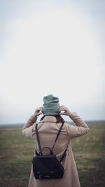 Rear view of woman photographing on field against sky