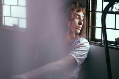 Depressed young woman sitting by window at home