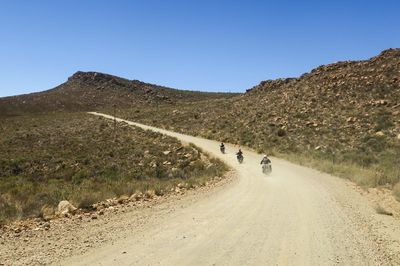 People on road by mountain against clear blue sky