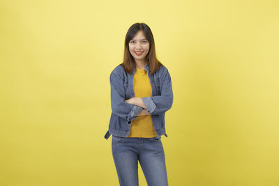 Portrait of smiling young woman against yellow background