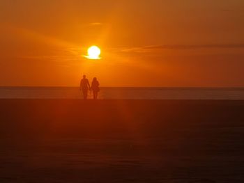 Silhouette people on beach against sky during sunset