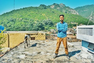 Portrait of young man standing on building terrace against mountain