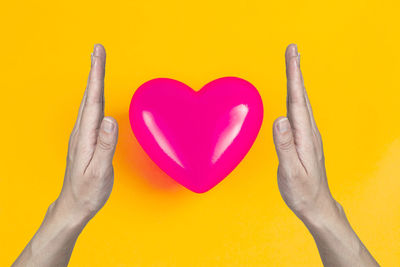 Close-up of hand holding heart shape against yellow background