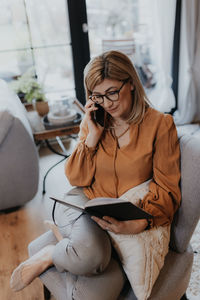 Woman reading diary while talking on phone at home