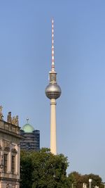 Low angle view of communications tower in city against clear blue sky