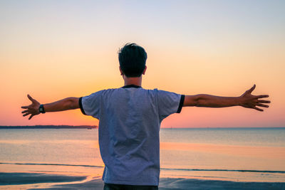 Rear view of man standing by sea against sky during sunset