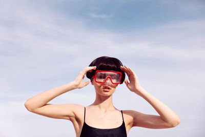 Young woman holding sunglasses against sky