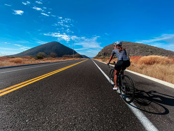 Man riding bicycle on road against mountain