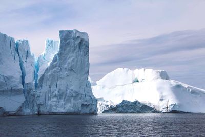 Scenic view of snow covered rock formation by sea against sky