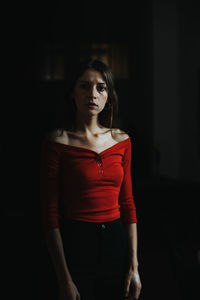 Portrait of young woman standing against black background