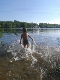 Rear view of shirtless boy standing in water