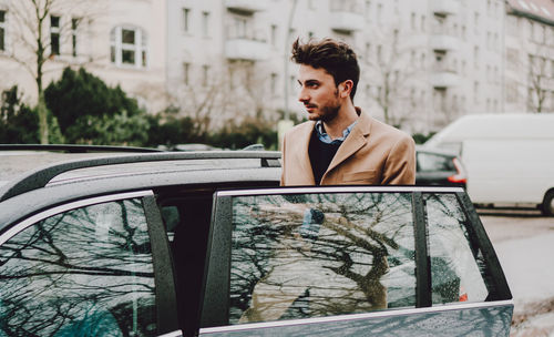 Young man entering wet car in city during rainy season