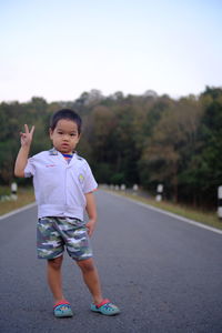 Portrait of boy gesturing peace sign while standing on road