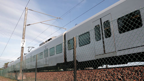 Low angle view of train by fence against sky