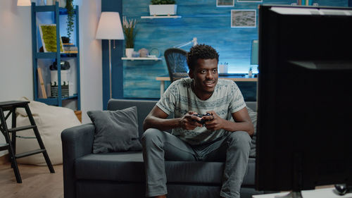 Man playing video game while sitting on sofa at home