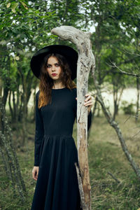 Portrait of young woman standing against trees