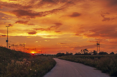 Road amidst trees against orange sky