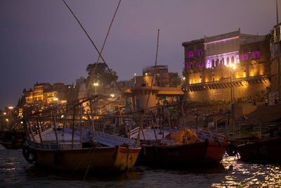 Sailboats moored on illuminated city by sea against sky at night