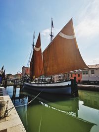 Sailboats moored on canal by building against sky