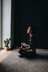 Side view of woman meditating in lotus position at home