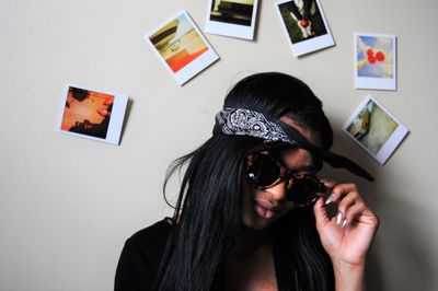 Close-up of woman wearing sunglasses against photographs stuck on wall