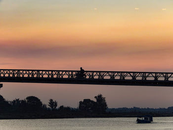 Silhouette bridge over sea against sky during sunset