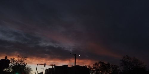 Low angle view of silhouette trees and buildings against dramatic sky