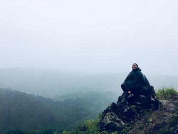 Woman sitting on mountain against sky