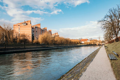 View of buildings by river against cloudy sky