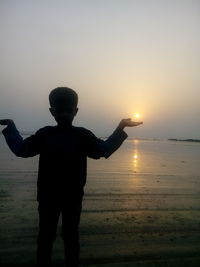 Silhouette boy standing at beach during sunset