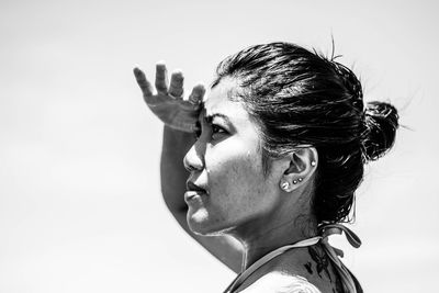 Close-up side view of woman shielding eyes while looking away against clear sky during sunny day