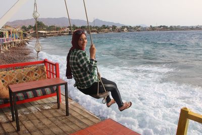 Portrait of smiling woman enjoying swing at beach