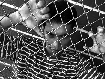 Close-up portrait of woman seen through chainlink fence