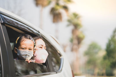 Mother with daughter wearing masks looking through car window
