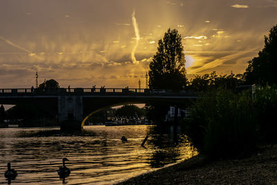 Silhouette bridge over river against sky at sunset