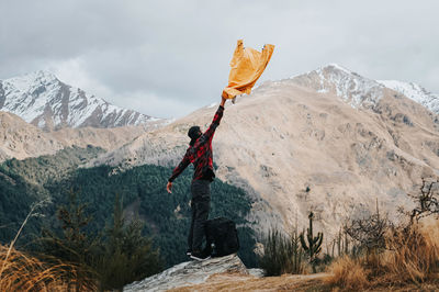 Man holding shirt while standing on rock against sky